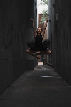 A ballet dancer in a dynamic leap captured dramatically in a city alleyway.