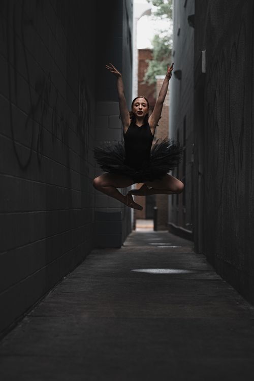 Free A ballet dancer in a dynamic leap captured dramatically in a city alleyway. Stock Photo