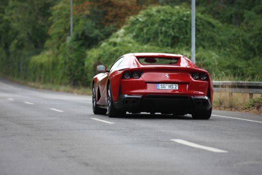 Sleek red Ferrari driving on a clear, open road surrounded by lush greenery.