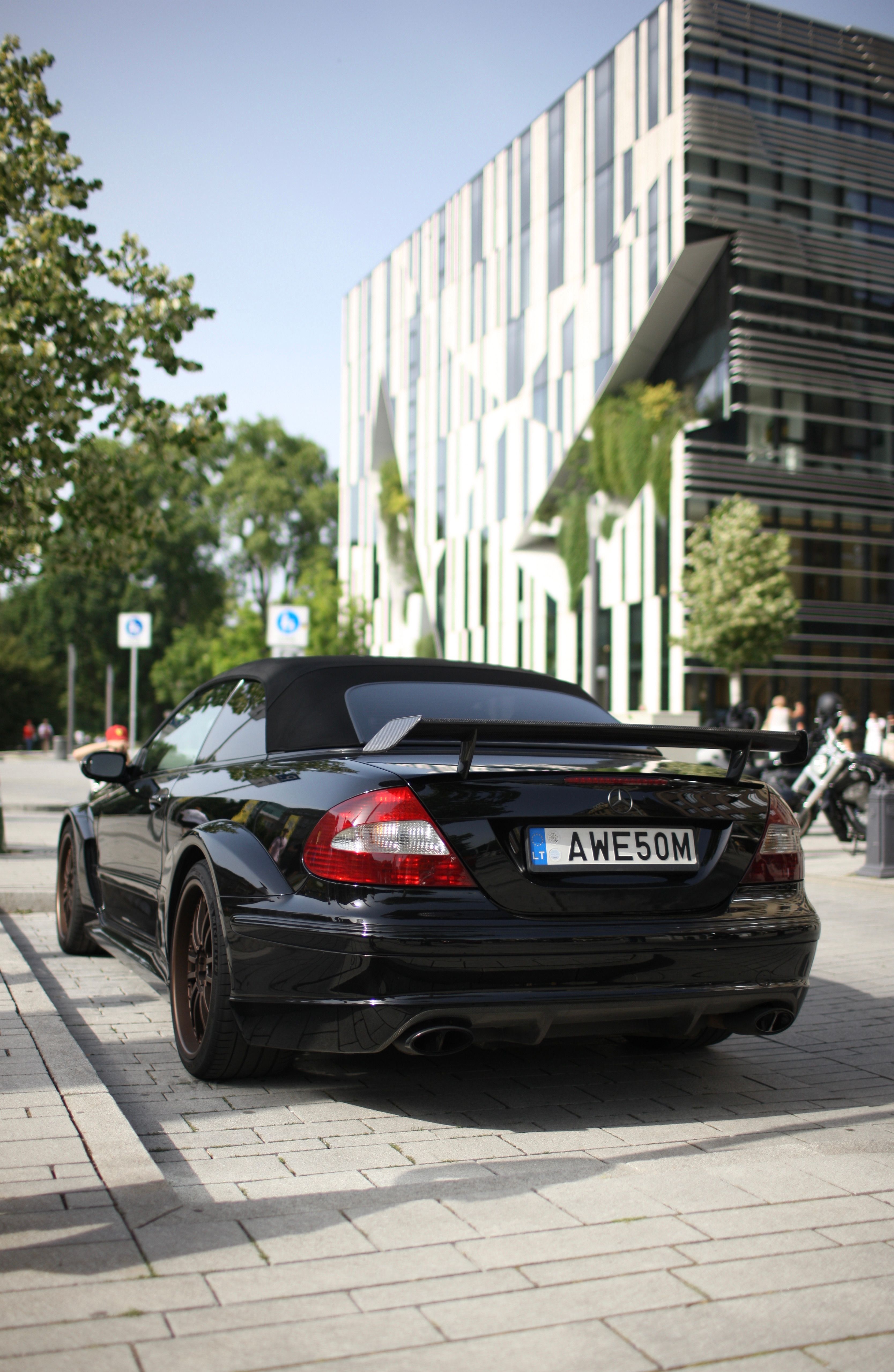 Black convertible luxury car parked on an urban street in front of a modern architecture building. Daytime setting.