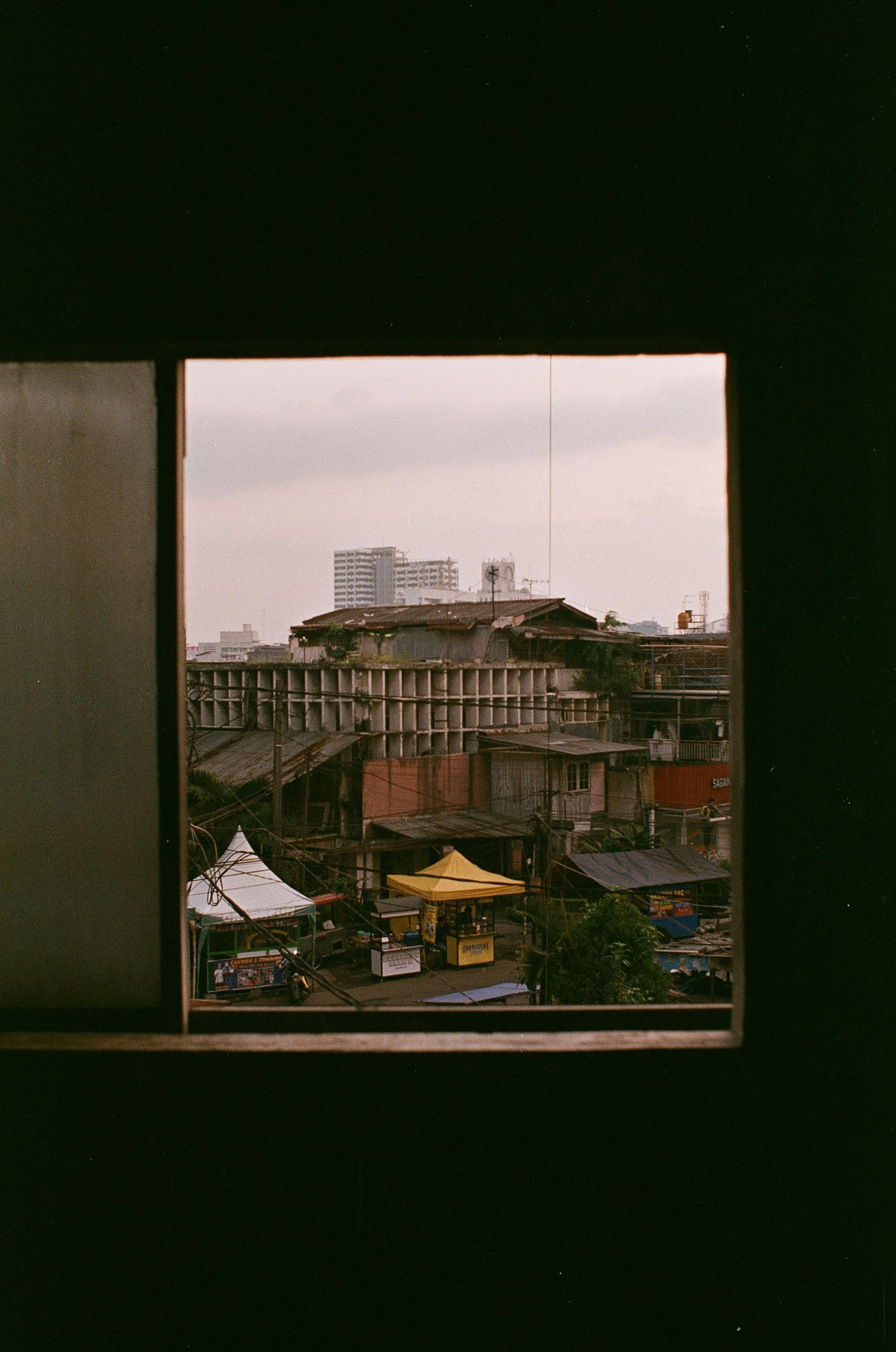 A cityscape framed by a window, showing rooftops and buildings in urban decay.