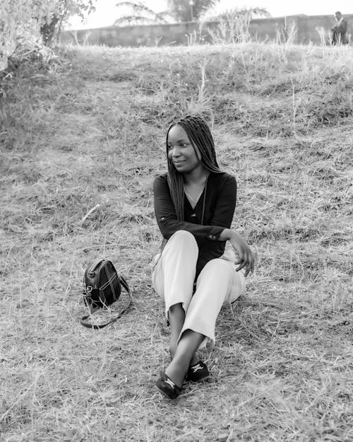 A Grayscale Photo of a Woman in Black Long Sleeves Sitting on Grass Field