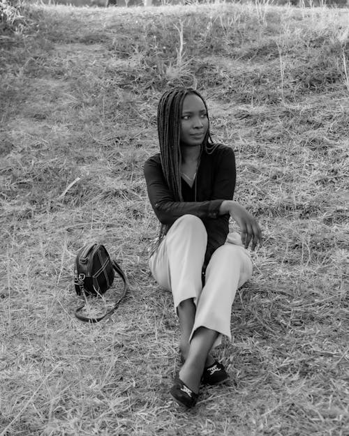 A Braided Hair Woman Sitting on Grass Field