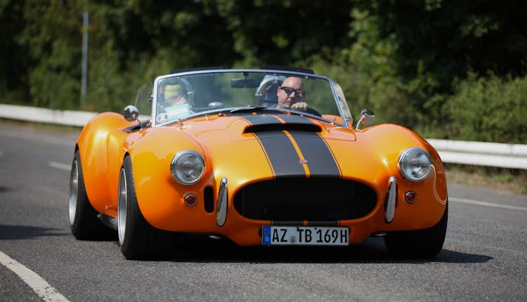 A Man Driving An Orange Car On The Road