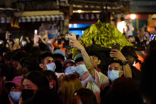 Free A large crowd wearing face masks captures the vibrant festival with cellphones. Stock Photo