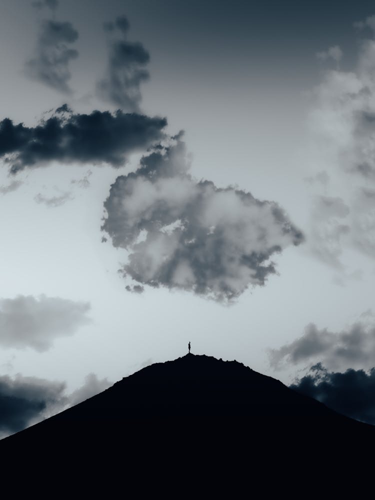 Silhouette Of A Person Standing On Top Of A Hill In Distance 