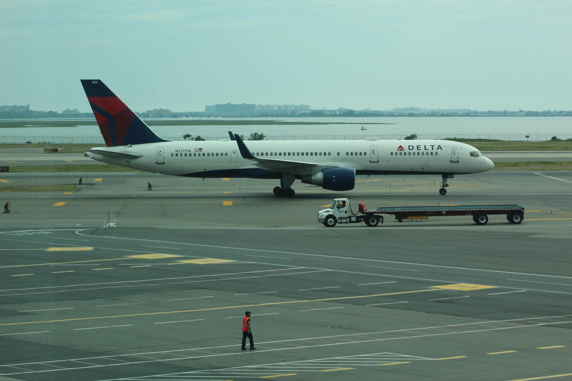 Person Standing Near Delta Airline Passenger Plane and Baggage Truck on Runway