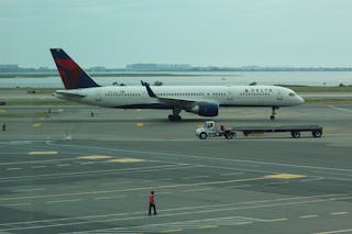 Person Standing Near Delta Airline Passenger Plane and Baggage Truck on Runway