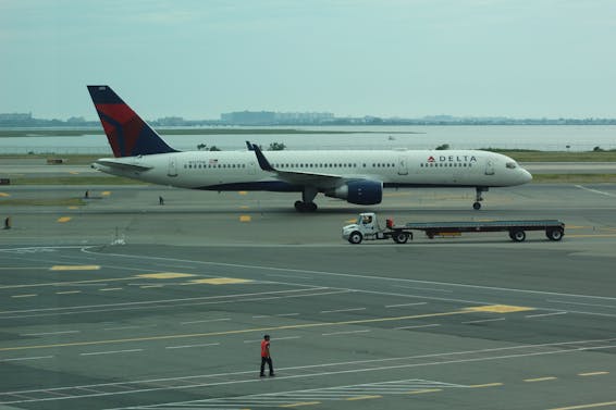 Person Standing Near Delta Airline Passenger Plane and Baggage Truck on Runway