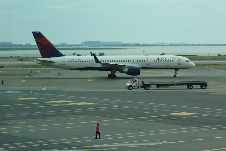 Person Standing Near Delta Airline Passenger Plane And Baggage Truck On Runway