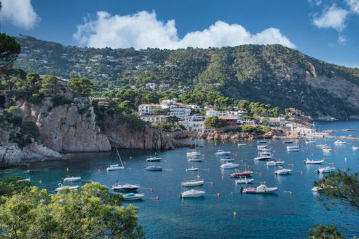 Tranquil Mediterranean bay with anchored boats, blue sea, and lush coastline.