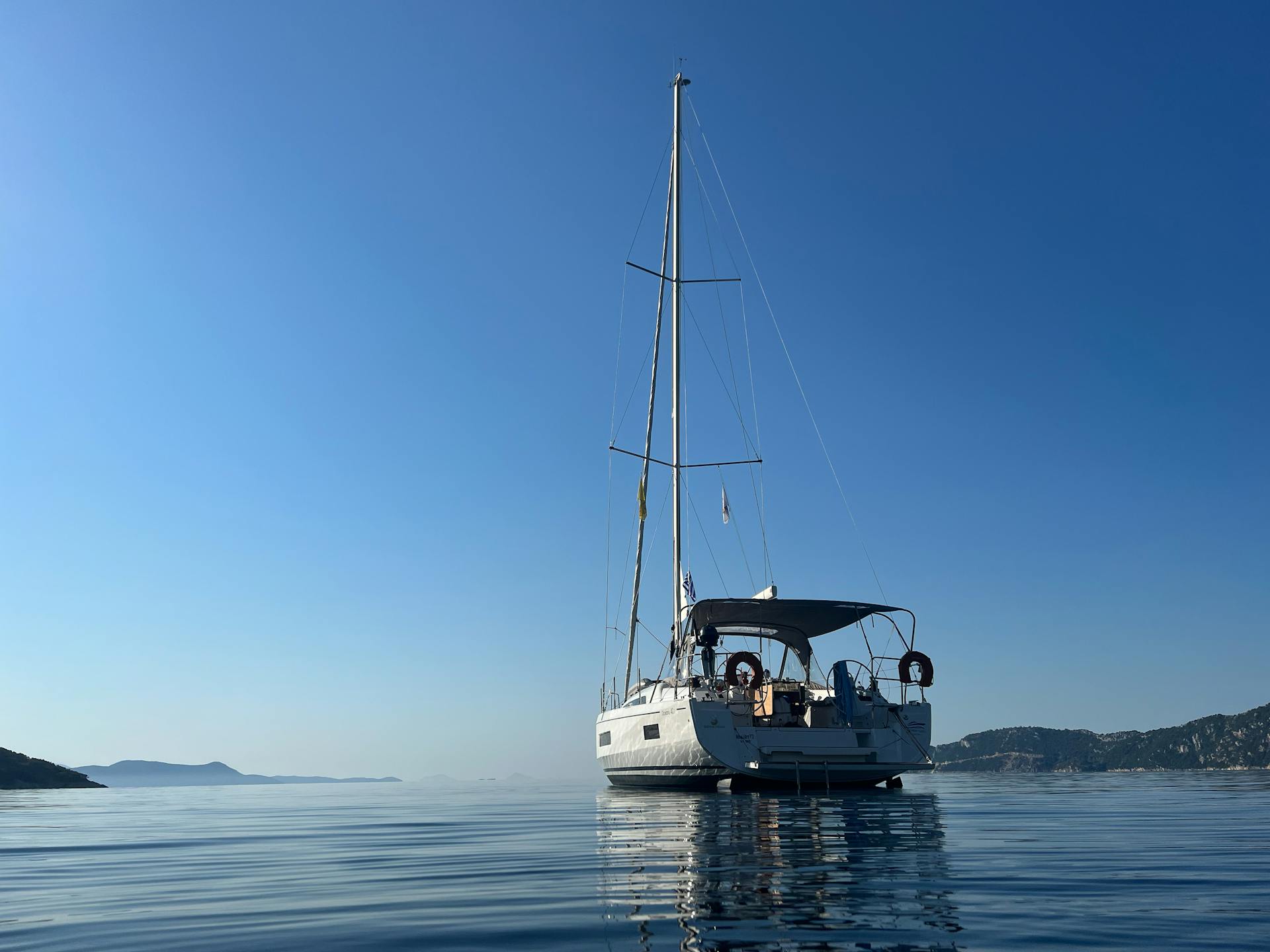 A tranquil scene of a yacht floating on calm water with a clear blue sky in Greece.