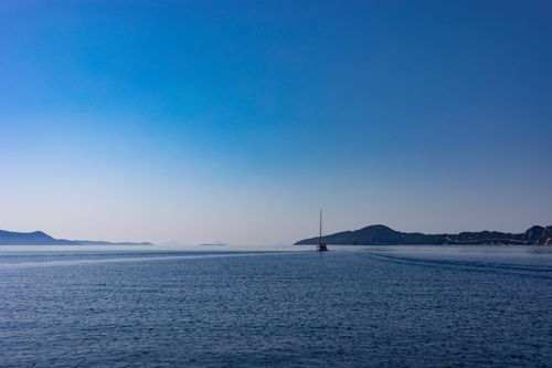Free A serene view of the Greek sea with a distant sailboat under a clear blue sky. Stock Photo