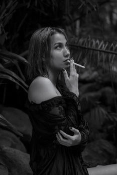 Black and white portrait of a woman smoking amidst lush foliage, creating a moody atmosphere.
