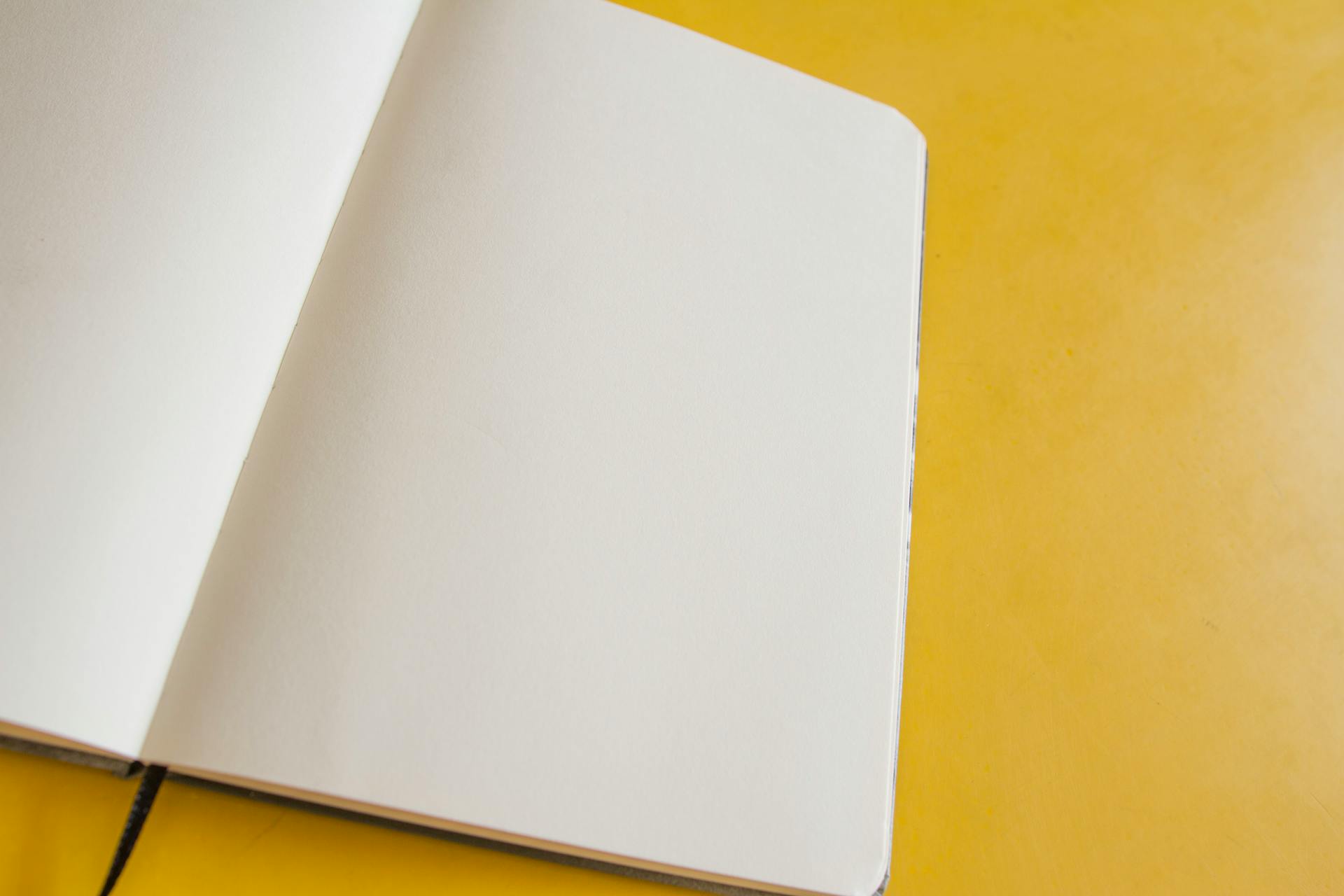 Top view of an open blank notebook on a vibrant yellow surface, perfect for creativity and planning.