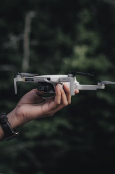 A close-up of a person holding a drone against a blurred forest background.