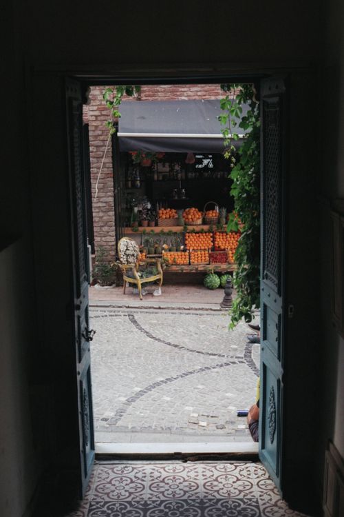 Free View through an ornate doorway to a cobblestone alley with vibrant fruit stall. Stock Photo