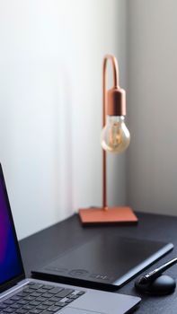 A sleek modern workspace featuring a laptop, digital tablet, and stylish lamp on a desk.