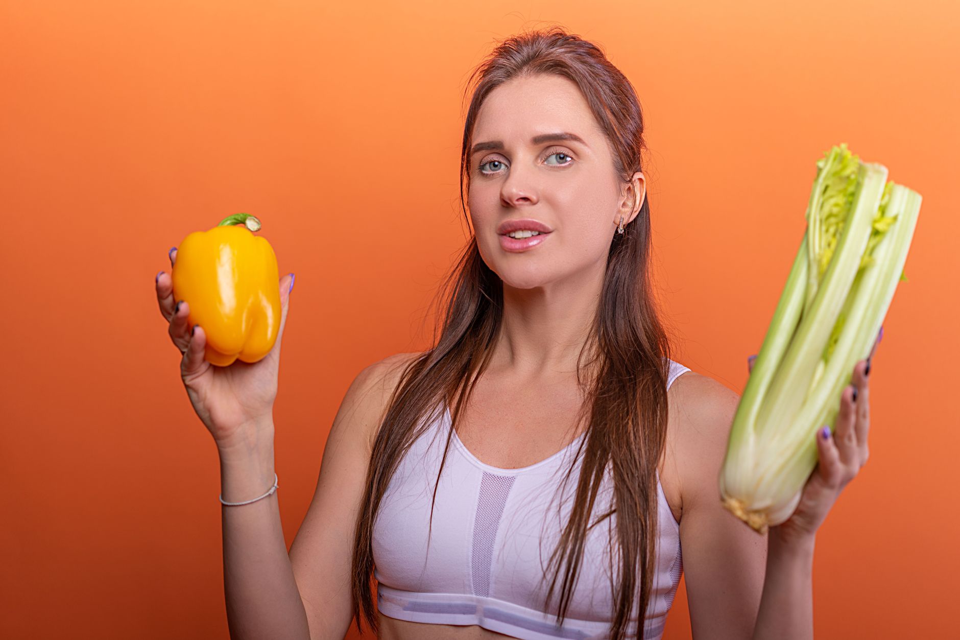 Woman holding yellow bell pepper and celery, showcasing healthy eating.