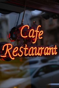 Close-up of a glowing neon Cafe Restaurant sign with urban reflections.