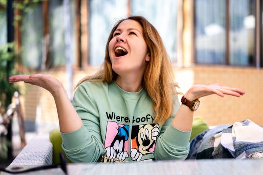 Young woman in cartoon sweater laughing with arms open outdoors.