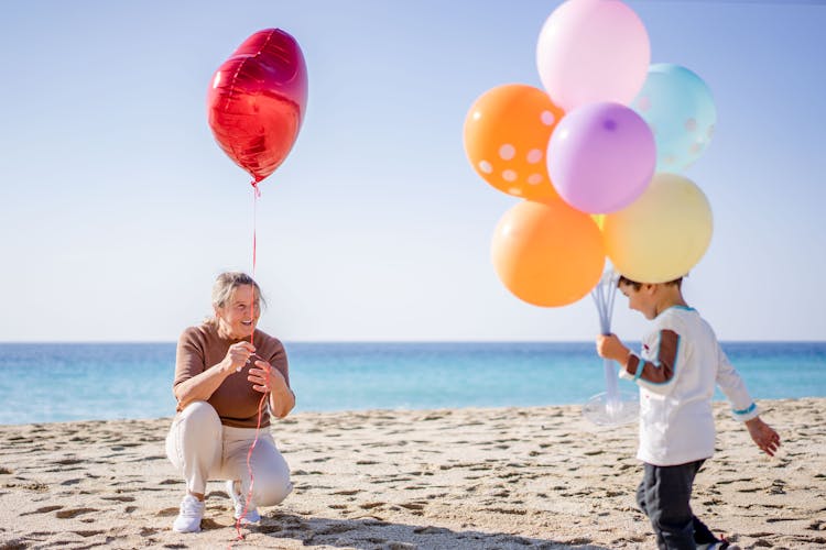 Woman And Boy Holding A Bunch Of Balloons On Beach Sand