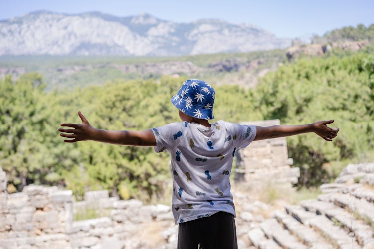 Young Boy Standing With Arms Open Above Ruins