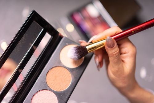 Free Hand with manicured nails using a makeup brush on a palette for cosmetic application. Stock Photo