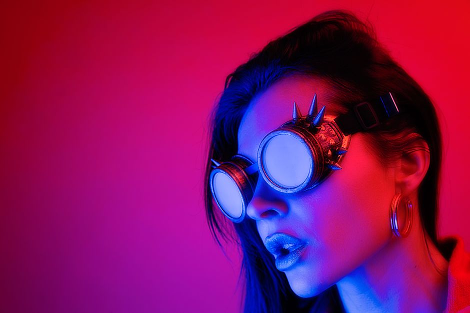Stylish portrait of a woman wearing spiked goggles in dramatic neon lighting.