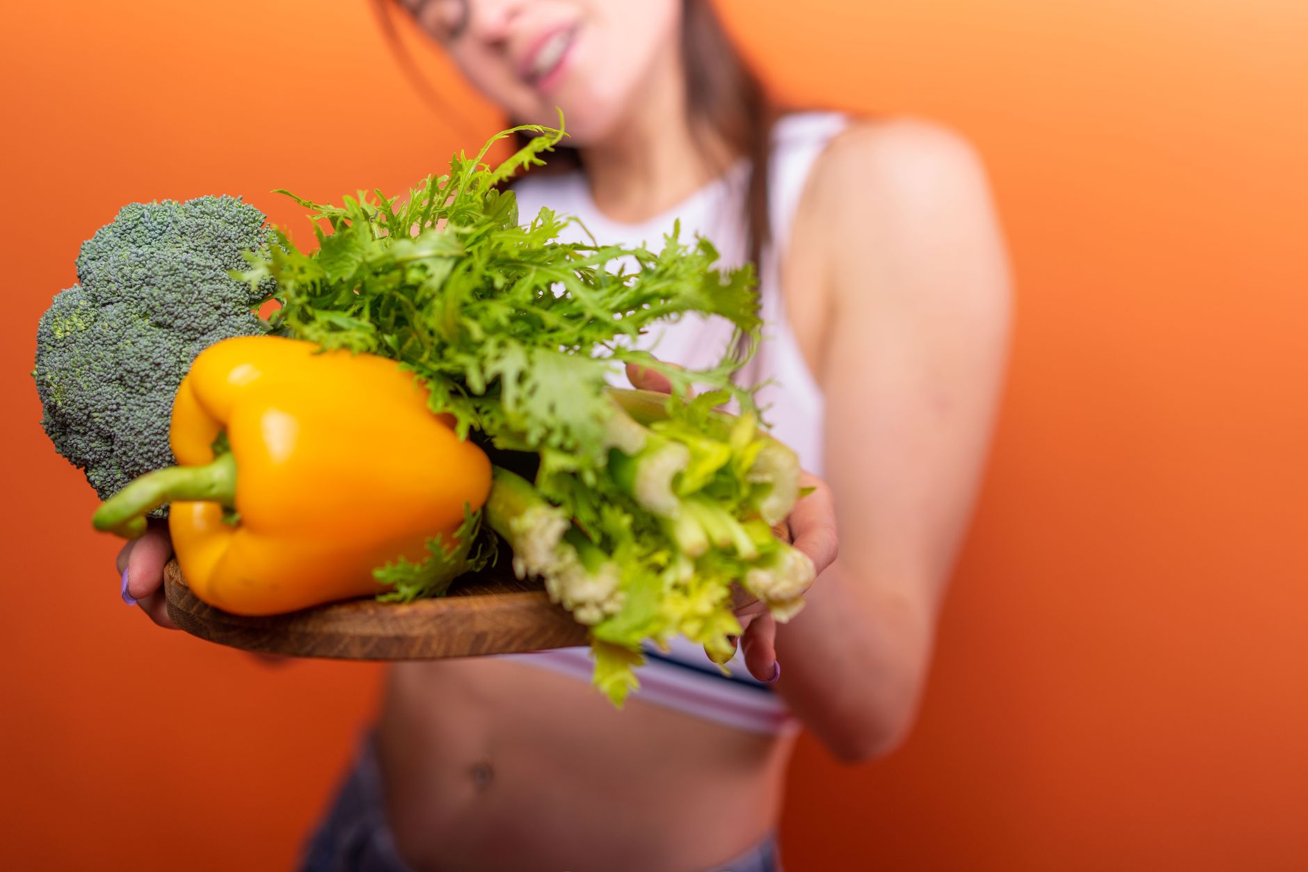 Healthy vegetables held by woman against orange background. Vibrant and fresh.