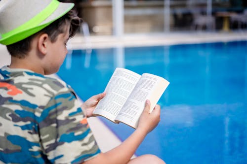 Boy Reading a Book by the Pool 