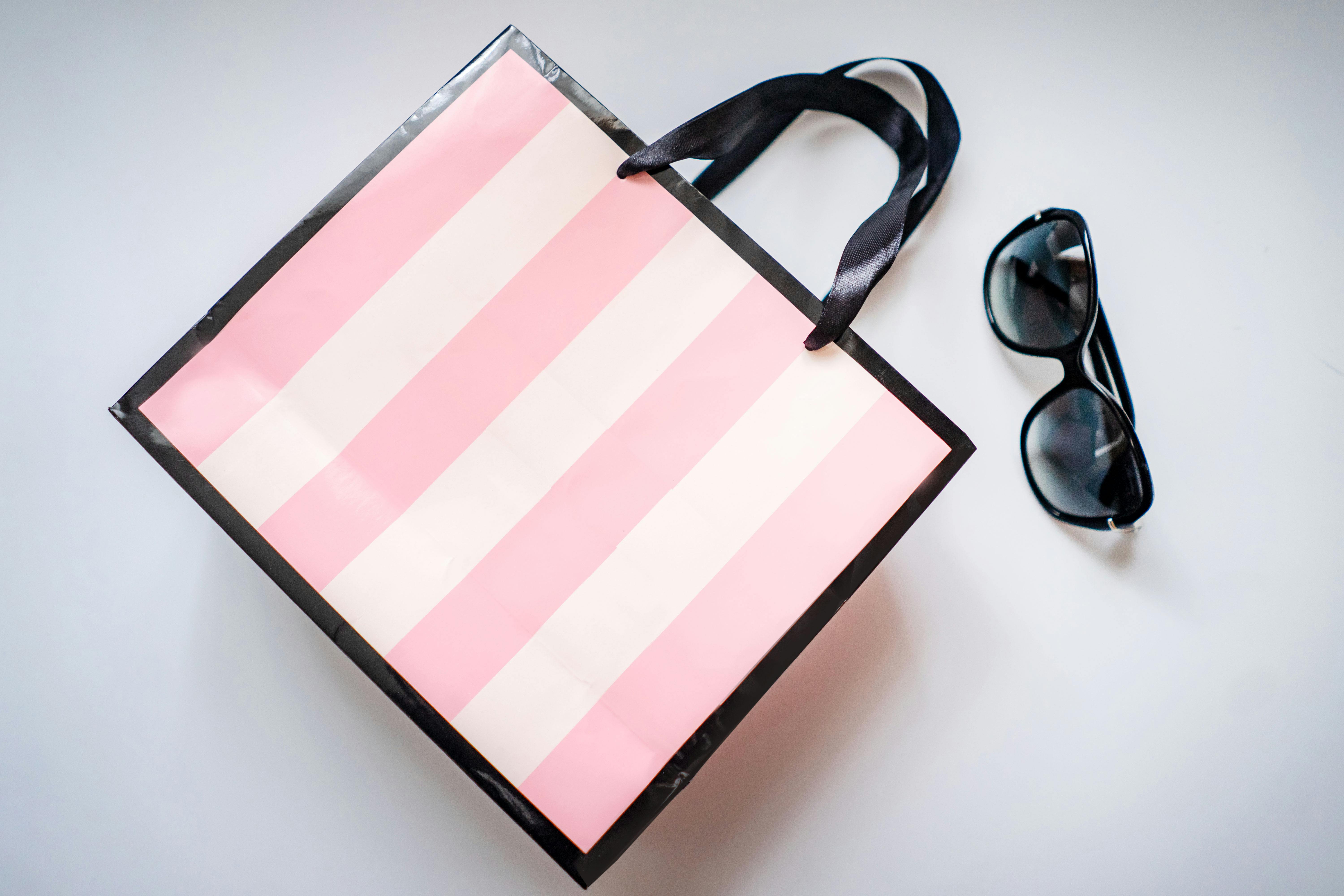 Top view of a pink striped shopping bag and sunglasses on a white surface, perfect for retail themes.