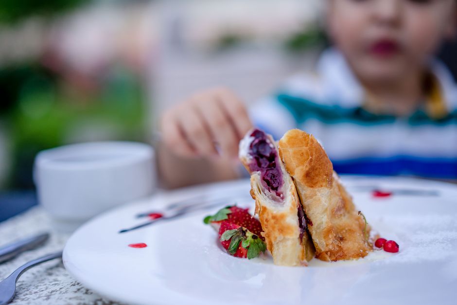 Photo by Atlantic Ambience on Pexels A child reaches for a delicious fruit-filled pastry dessert on a white plate with strawberries. - Photo by Atlantic Ambience on Pexels