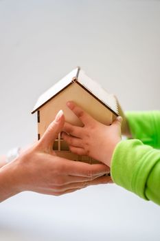 Close-up of mother and child holding a small wooden model house, symbolizing family and home.