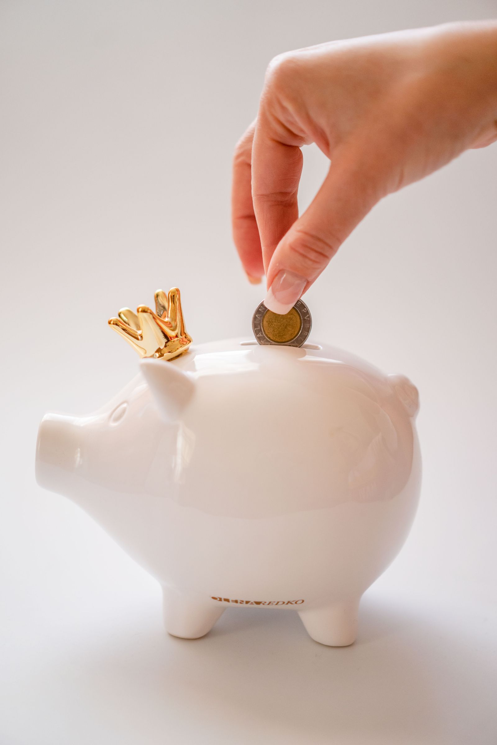 Hand placing a coin into a white piggy bank