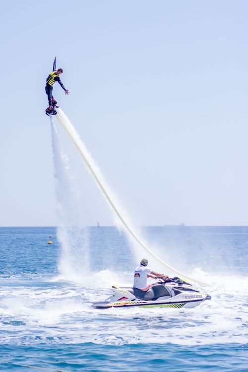 Free Thrilling flyboarding action as a man performs a high stunt over the sea with a jet ski nearby. Stock Photo