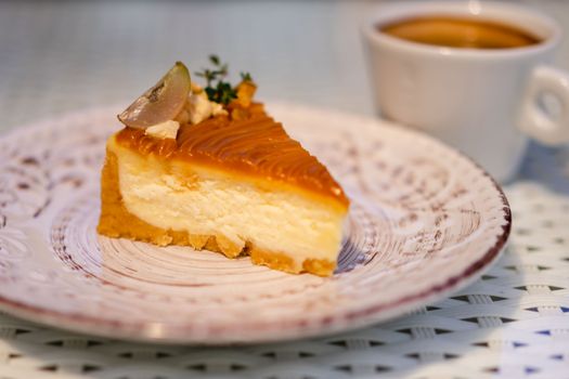 Close-up of a caramel cheesecake slice on a patterned plate with a cup of coffee.