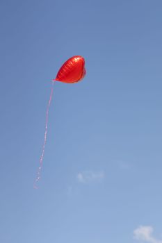 A vibrant red heart-shaped balloon soaring against a clear blue sky symbolizing love and freedom.