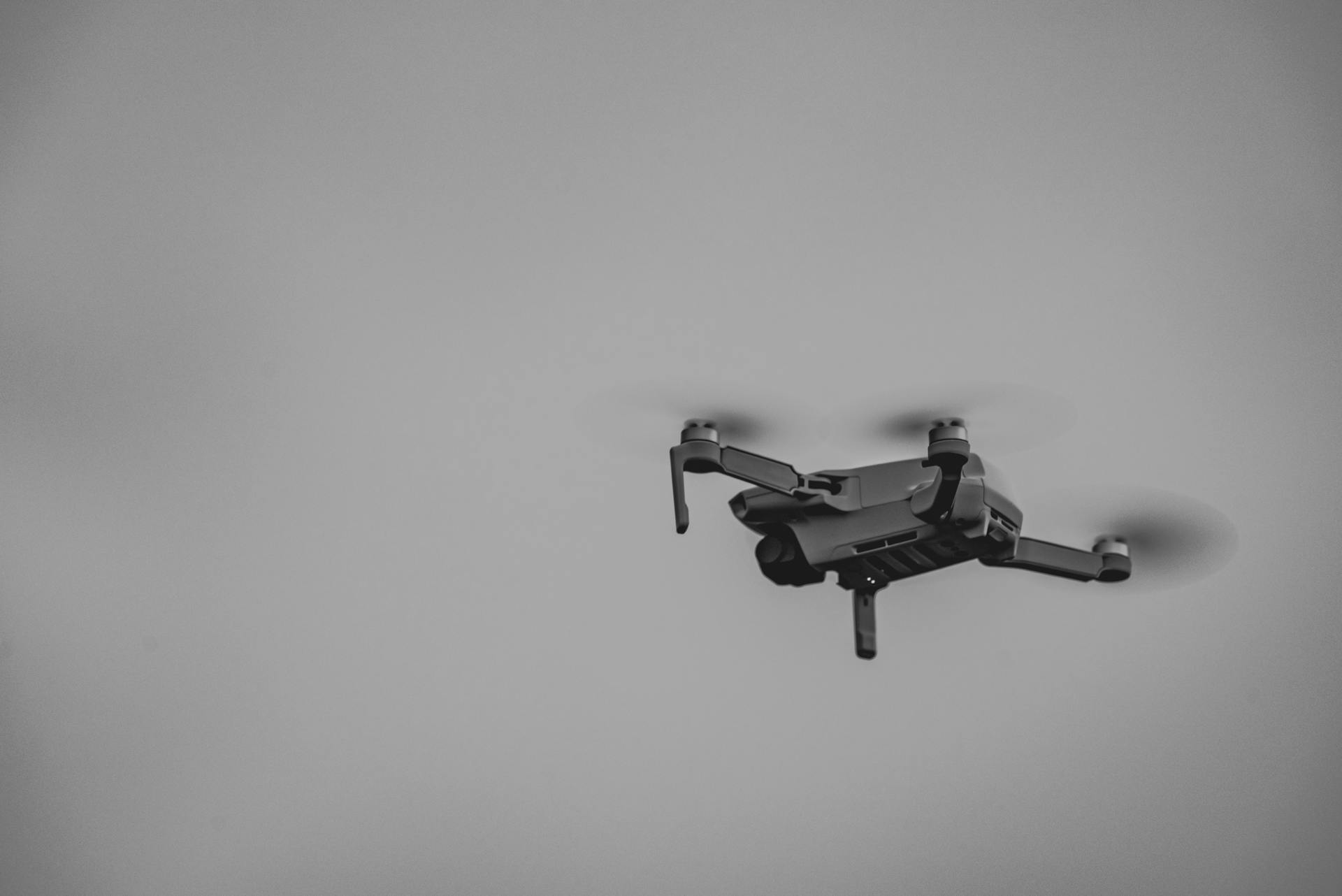 A monochrome image of a drone flying against a gray sky, showcasing modern technology.