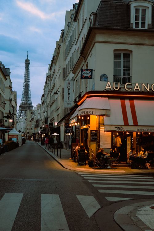 Free Vibrant Paris street scene at twilight featuring a cozy cafe and the iconic Eiffel Tower in the background. Stock Photo
