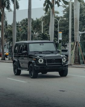 A black Mercedes-Benz SUV drives on a city street surrounded by palm trees, showcasing luxury and elegance.