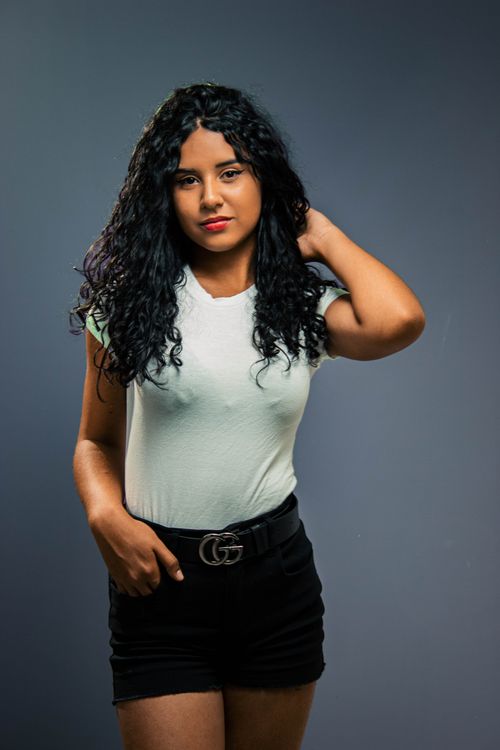 Free A confident woman with curly hair poses in a white t-shirt and black skirt in a studio setting. Stock Photo