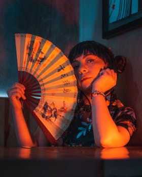 A woman holding a traditional Japanese fan under warm ambient lighting indoors.