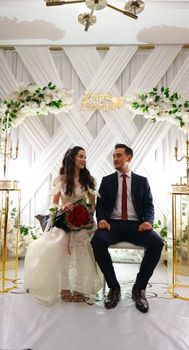 Bride and groom sitting elegantly at a wedding ceremony with floral decor.