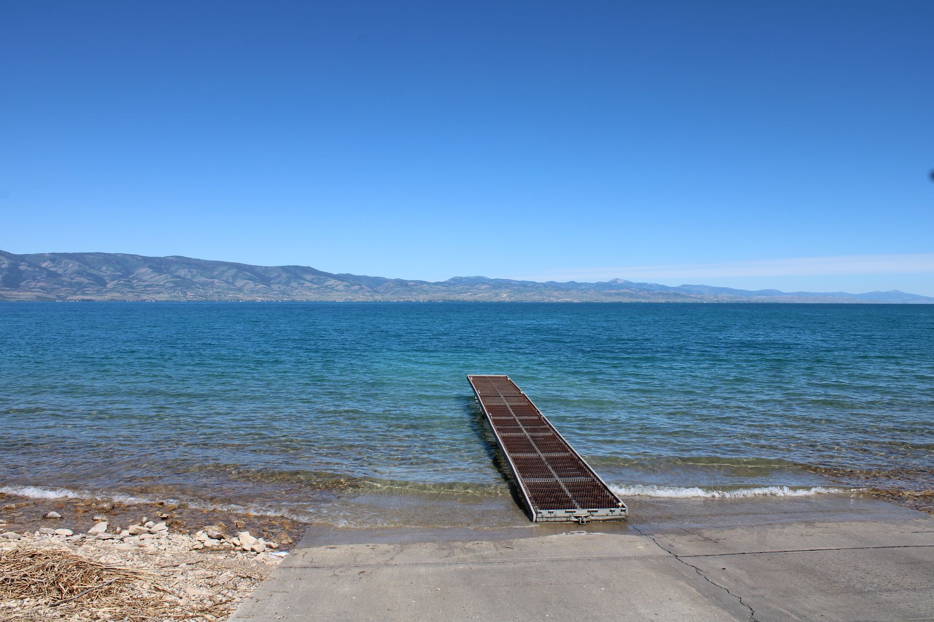 Serene view of a pier going into a clear blue lake with mountain backdrop.