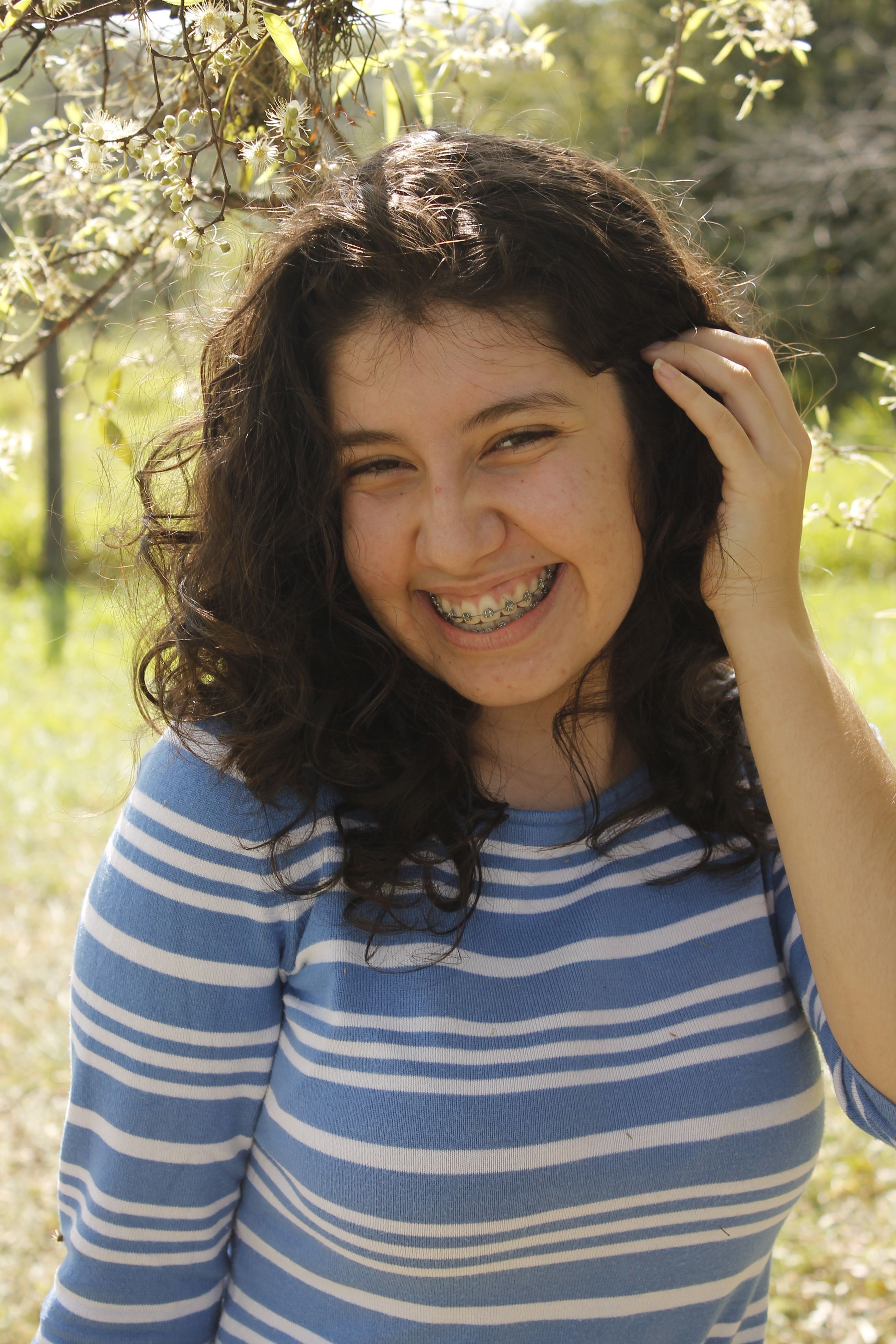 Smiling brunette teen with braces and curly hair enjoying a sunny day outdoors in Caacupé, Paraguay.