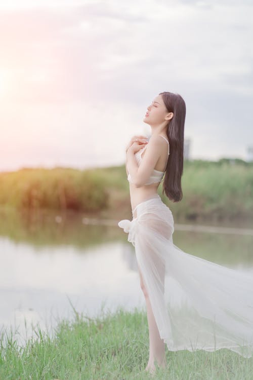 Woman in White Lingerie Standing on Green Grass Near Water
