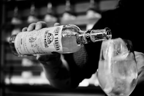 Free Grayscale Photography of Person Pouring Alcoholic Drink on Clear Glass Stock Photo