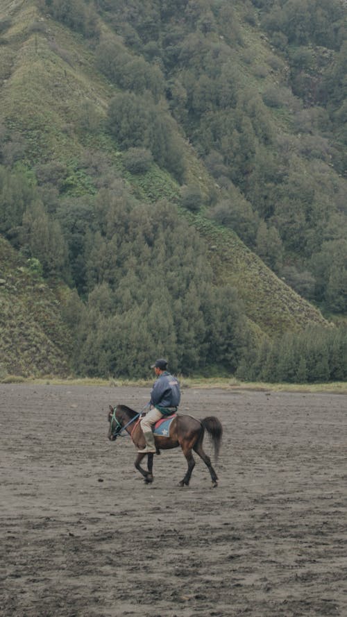 Man Riding a Horse Near Green Mountain