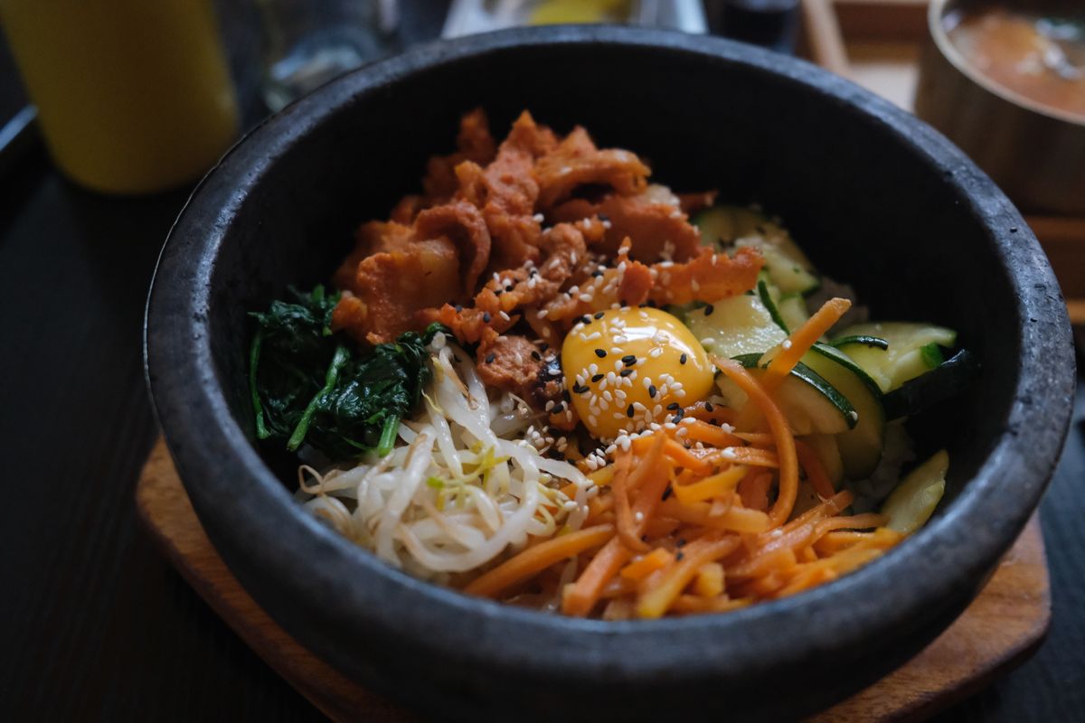 Hot stone bowl bibimbap with spicy pork, raw egg yolk, sprouts, carrot, zucchini and spinach
